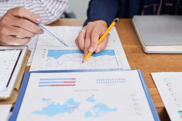 Two people hold pencils over charts and graphs.