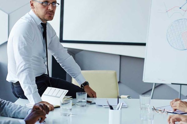 A group of people discussing a chart, sitting at a board room table.